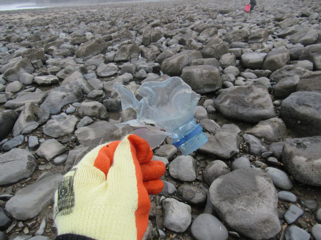 Gloved had holding the top of a plastic bottle, destroyed by the elements
