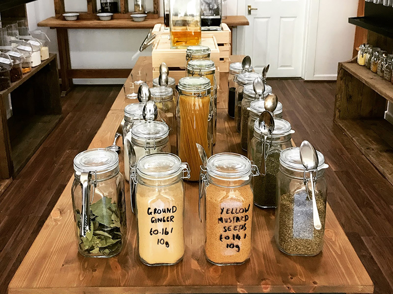 Table in a shop with glass jars containing various items such as ginger and mustard seeds