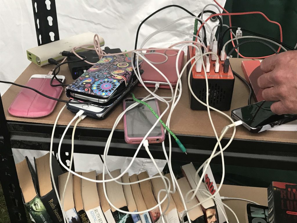 A number of phones tangled among chords sits next to a charging station on a bookshelf, surrounded by printed books.