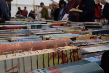 A line of print book bindings facing up on a table, with people in the background leaning over and looking at them