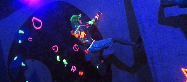 A climber tackles the neon holds in darkness.