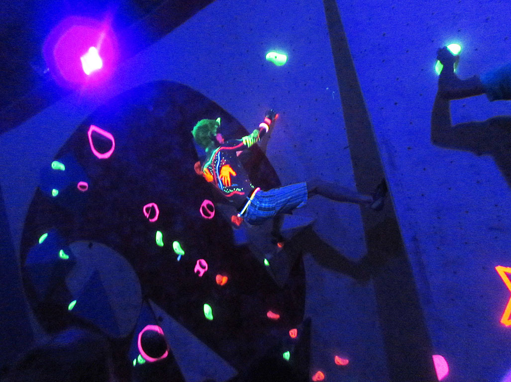 A climber tackles the neon holds in darkness.